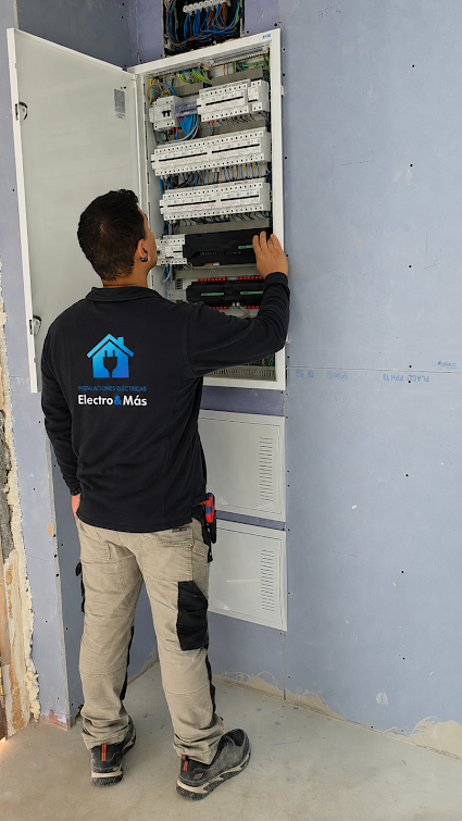 Técnico de Electro & Más con ropa de trabajo corporativa realizando una instalación eléctrica en un cuadro abierto durante una obra