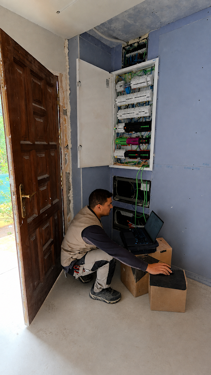 Técnico de Electro & Más configurando con ordenador portátil un sistema eléctrico junto al cuadro de distribución