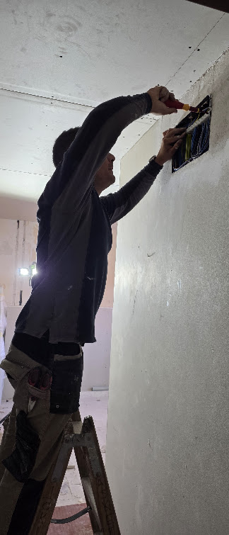 Técnico electricista instalando cuadro eléctrico desde escalera durante una intervención de urgencia